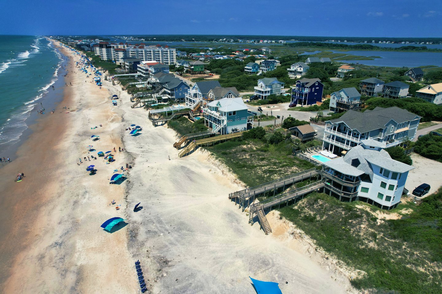 Houses line a sandy beach beside the blue ocean.