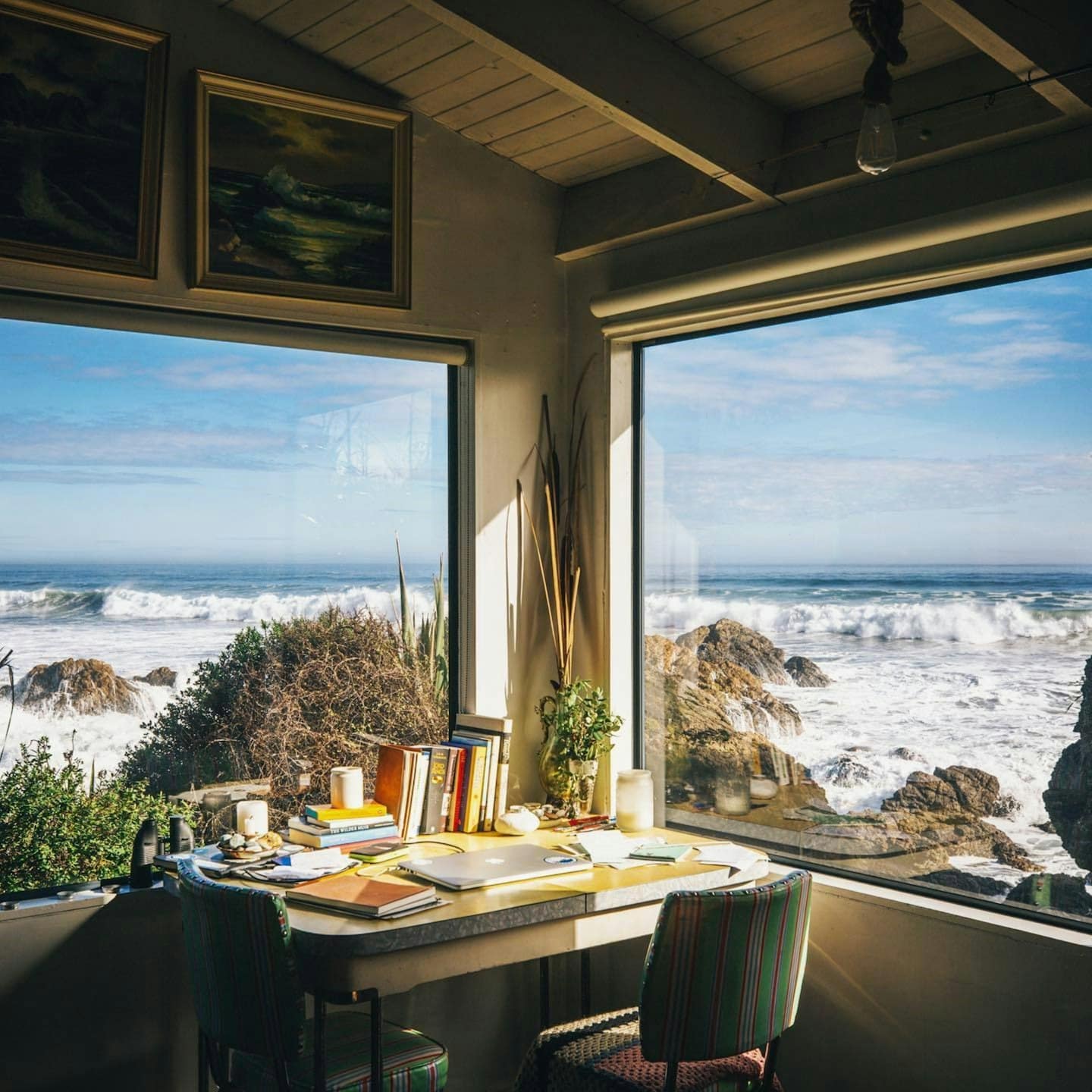 Home office with desk and chairs facing a coastal view.